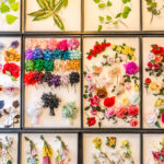 Bunte künstliche Blumen und Blätter in einem Raster aus schwarz umrandeten Rahmen mit verschiedenen Formen, Größen und Farbtönen auf weißem Hintergrund.